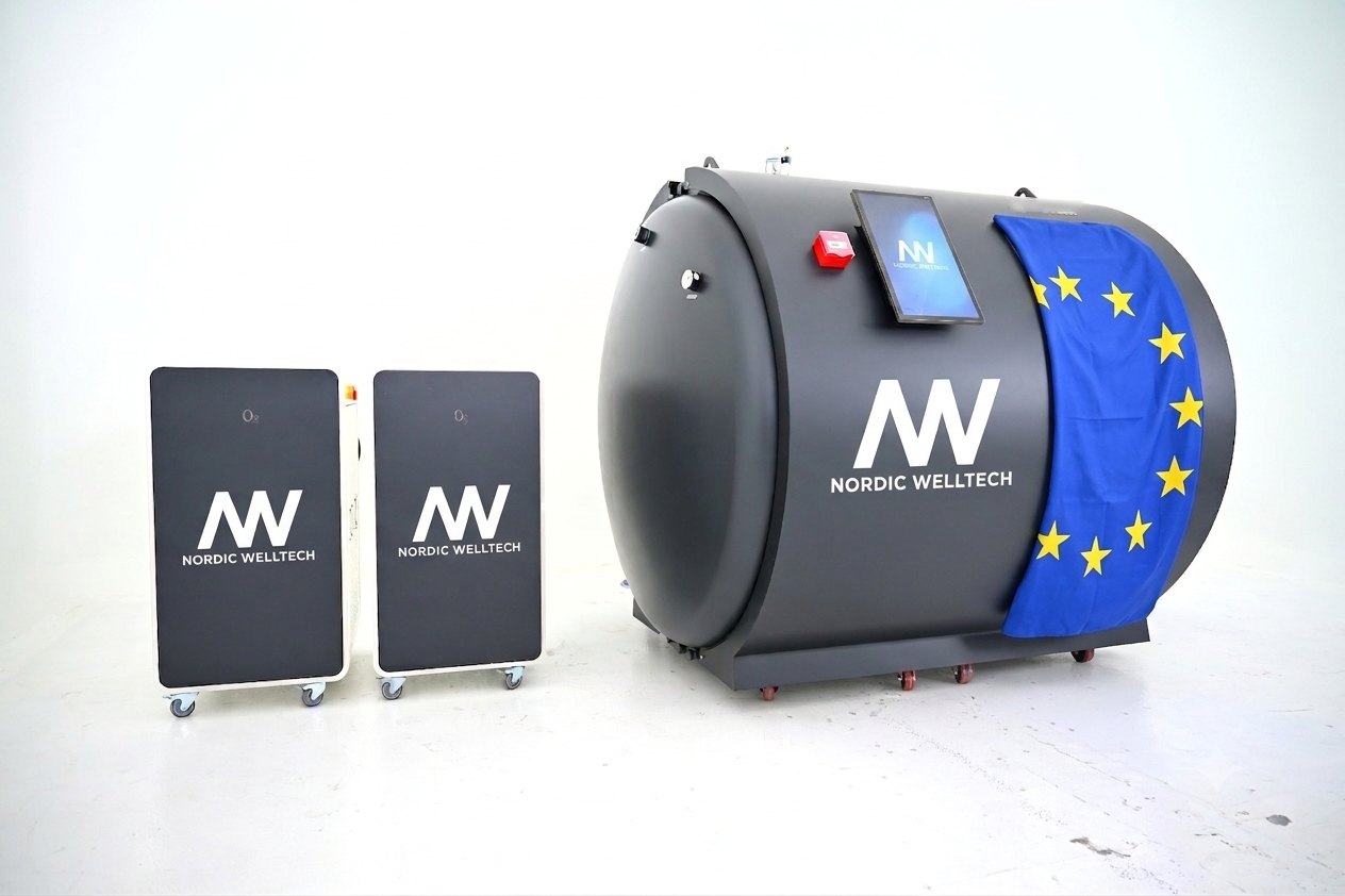 Nordic Welltech hyperbaric oxygen chamber draped with the EU flag, next to two oxygen concentrators